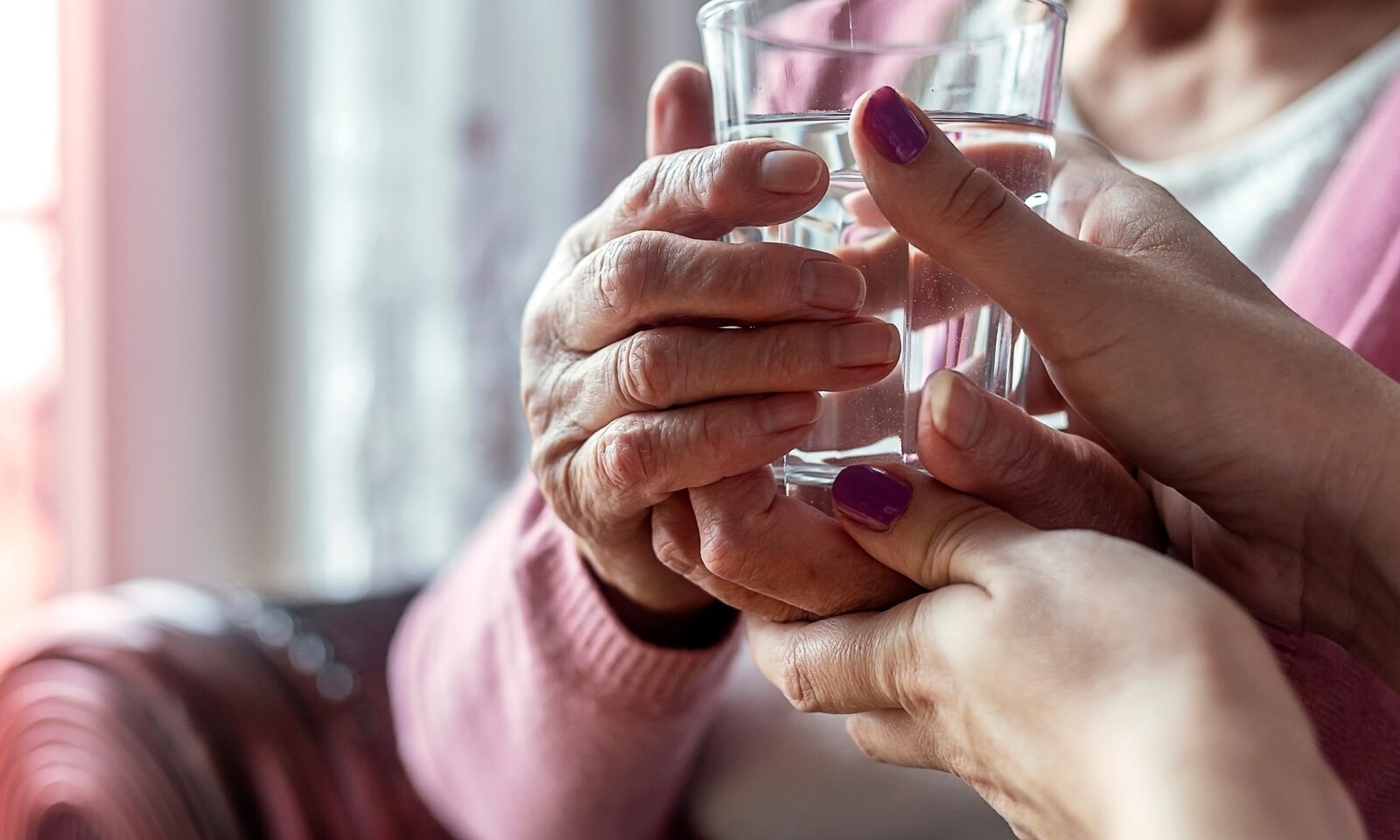 A pair of hands holding a glass of water gently steadied by a younger pair of hands.